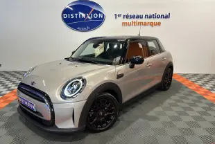 Vue 3/4 avant droite d'une MINI Cooper 5 portes gris clair avec toit noir et jantes noires dans un showroom.