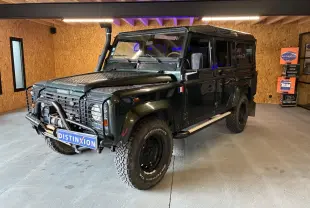 Land Rover Defender 110 vert vue 3/4 avant droit avec treuil, plaques de protection et pneus tout-terrain.