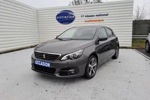 Peugeot 308 gris vue 3/4 avant droit avec jantes alliage et calandre chromée sur parking extérieur.