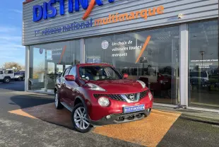 Nissan Juke rouge 2017 en 3/4 avant droit, stationné devant un showroom avec plaques Distinxion visibles.