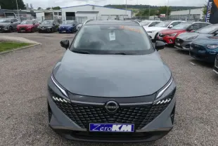 Vue avant d'un Nissan Qashqai gris métallisé avec calandre noire et feux LED distinctifs, stationné en extérieur.