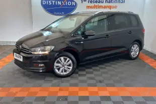 Vue 3/4 avant d'un Volkswagen Touran noir garé en intérieur sur sol à damiers gris et orange, avec logo Distinxion en arrière-plan.