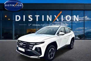 Vue 3/4 avant droite du Hyundai Tucson blanc 2026 avec calandre noire et jantes alliage 17 pouces devant un showroom Distinxion.