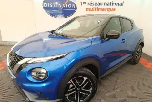 Nissan Juke bleu en 3/4 avant droit, avec toit noir et jantes alliage bicolores visibles en intérieur showroom.
