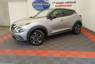 Nissan Juke gris clair vu de profil droit, avec jantes noires et toit noir contrastant, dans un showroom multimarque.