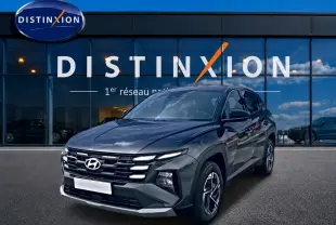 Hyundai Tucson 1.6 t-gdi 239 hybride gris ecotronique en 3/4 avant droit devant une vitrine Distinxion.