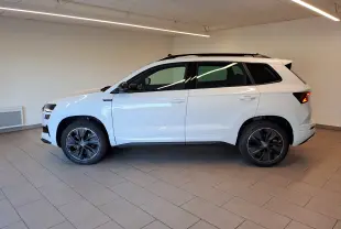 Vue de profil côté gauche d’un Skoda Karoq blanc lune 2025 avec jantes noires et toit ouvrant panoramique.