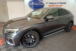 Audi Q5 gris clair 2023 en 3/4 avant droit, avec jantes noires et détails chromés, dans un showroom intérieur.