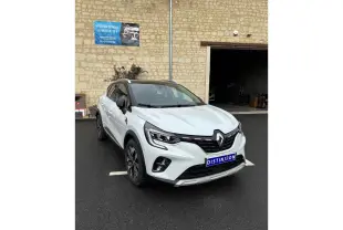 Renault Captur blanc en 3/4 avant droit, avec toit noir et détails noirs contrastants sur un parking extérieur.