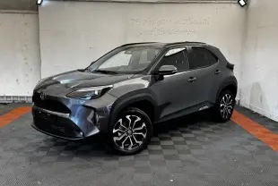 Toyota Yaris Cross 2026 gris foncé vue 3/4 avant avec jantes alliage et toit noir dans un garage.
