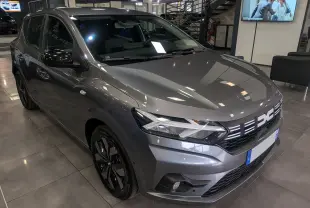 Vue 3/4 avant d'une Dacia Sandero TCe 90 CH Journey gris schiste avec jantes noires et calandre lumineuse en showroom.