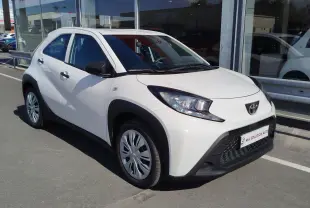 Toyota Aygo X blanc pur vue 3/4 avant droit, avec protections noires autour des passages de roues et calandre noire.