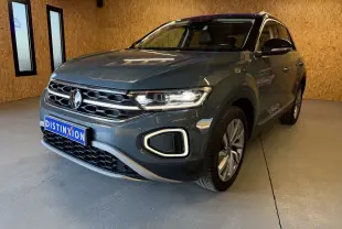 Vue frontale d'un Volkswagen T-Roc bleu 2022 avec calandre chromée et phares allumés en intérieur showroom.