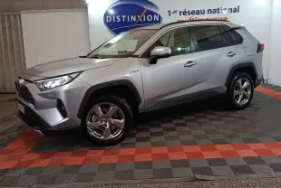 Toyota RAV4 Hybride gris clair vu de profil droit en intérieur, avec jantes alliage et logo Distinxion en arrière-plan.