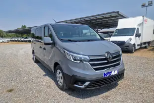 Vue 3/4 avant droit d’un Renault Trafic Combi gris urbain stationné sur un sol gravillonné avec un abri solaire en arrière-plan.
