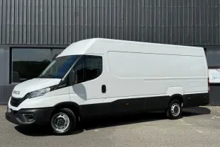 Fourgon Iveco Daily blanc vu de profil côté gauche, avec pare-chocs et bas de caisse noirs, stationné devant un bâtiment industriel.