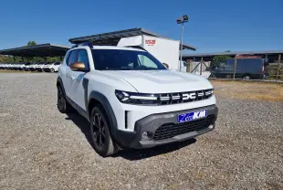 Vue 3/4 avant gauche d'un Dacia Duster blanc 2026 avec rétroviseurs bronze et calandre distinctive noire.
