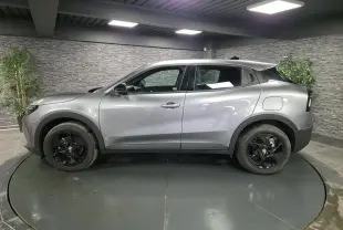 Vue de profil côté gauche d'une Alfa Romeo Junior 1.2 Ibrida gris métallisé avec jantes alliage noires dans un showroom.