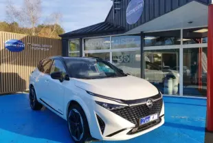 Vue 3/4 avant d'un Nissan Qashqai blanc nacré avec toit noir, stationné devant un showroom Distinxion.