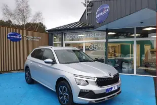 Vue 3/4 avant gauche d’un Skoda Kamiq gris diamant métallisé avec jantes alu et calandre noire devant un showroom.