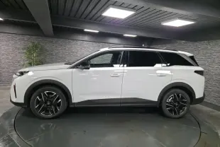 Profil droit du Peugeot 5008 blanc 2025 avec jantes alliage noires et barres de toit noires brillantes.