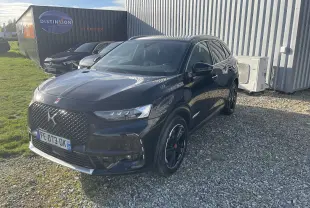 DS7 Crossback noir vue 3/4 avant droit, avec calandre distinctive et jantes noires, stationné sur gravier devant un bâtiment.