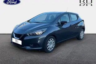 Nissan Micra gris acier vue 3/4 avant droit, avec jantes enjoliveurs et feux avant allumés.