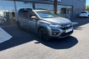 Dacia Jogger gris schiste en 3/4 avant droit, avec jantes noires et détails noirs sur la calandre et les bas de caisse.