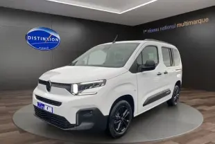 Vue 3/4 avant droite d'un Citroën Berlingo blanc 2025 avec phares allumés et jantes noires en showroom.