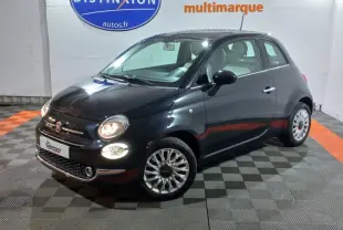 Vue 3/4 avant droite d'une Fiat 500 noire avec phares allumés dans un showroom intérieur.