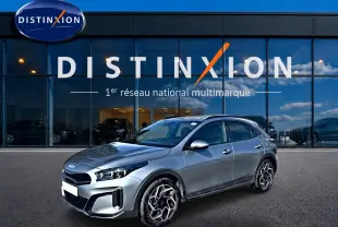 KIA Xceed gris en 3/4 avant droit, avec jantes alu distinctives, stationné devant une vitrine Distinxion.