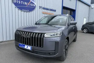 Vue 3/4 avant du JAECOO J5 gris Phantom avec calandre verticale noire et phares LED fins, stationné devant un bâtiment.