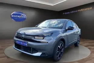 Vue 3/4 avant d'une Citroën C4 hybride gris clair avec jantes noires et détails chromés, sur podium intérieur.
