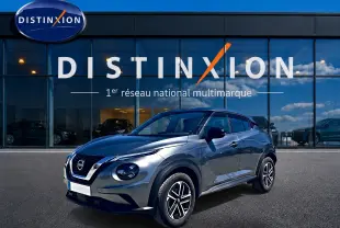 Nissan Juke gris 3/4 avant droit avec jantes alu, garé devant une vitrine Distinxion.
