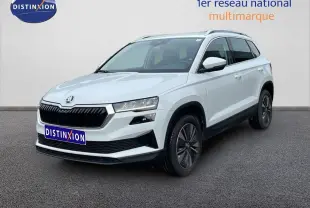 Vue 3/4 avant d'un Skoda Karoq blanc glacier avec jantes bi-ton et barres de toit alu sur fond neutre.