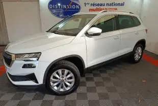 Vue 3/4 avant droite d’un Skoda Karoq blanc 2024, avec jantes alliage et rétroviseurs blancs, en intérieur showroom.