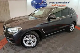 BMW X3 xDrive30e gris foncé vue 3/4 avant droit avec phares allumés dans un showroom intérieur.