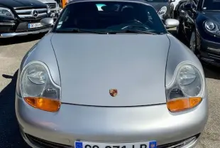 Vue frontale d'une Porsche Boxster 986 gris clair de 2001, avec phares ovales et plaque d'immatriculation française visible.