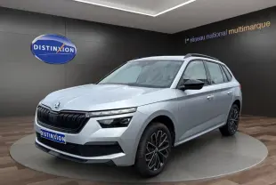 Vue 3/4 avant d'un Skoda Kamiq gris clair avec jantes bi-ton et rétroviseurs noirs dans un showroom.