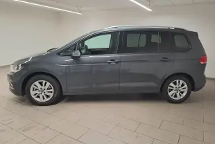 Vue de profil côté gauche d'un Volkswagen Touran gris dauphin 2024 dans un intérieur neutre, sans attelage visible.