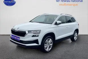 Vue 3/4 avant droite d’un Skoda Karoq blanc glacial avec jantes alu et barres de toit visibles.