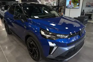 Renault Captur E-Tech hybride 2026 bleu Iron avec toit noir, vue 3/4 avant droit en intérieur showroom.
