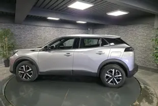 Peugeot 2008 gris en profil droit, jantes noires et argent, toit noir contrastant, dans un showroom intérieur.