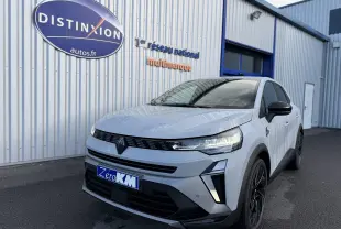 Vue 3/4 avant d'une Renault Symbioz gris rafale avec calandre noire et jantes noires devant un bâtiment industriel.