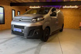 Vue 3/4 avant droit d'un Citroën Jumpy gris métallisé 2022 dans un garage en bois, avec calandre noire et jantes foncées.