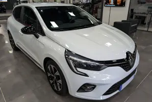 Renault Clio V blanc glacier vue 3/4 avant droit, avec jantes noires et rétroviseurs noirs brillants en intérieur showroom.