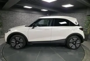 Vue latérale droite d'une Smart #1 électrique blanche avec jantes design et toit contrasté noir en intérieur showroom.