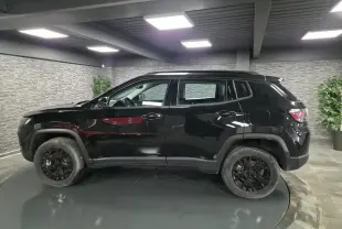 Vue de profil côté gauche d'un Jeep Compass noir avec jantes noires et garde au sol surélevée dans un showroom.