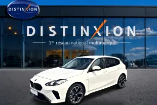 BMW Série 1 blanche vue en 3/4 avant droit, avec jantes alliage noires et calandre M Sport devant un showroom Distinxion.