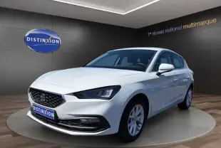 Vue 3/4 avant d'une SEAT Leon blanche 2025, avec calandre noire et phares LED, sur podium intérieur showroom.